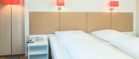 A hotel room with a bed, bedside tables, a telephone, and two wall-mounted lamps.
