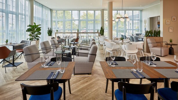 Un restaurante moderno con techos altos, ventanas amplias y una variedad de opciones de asientos, incluyendo mesas y sillas.