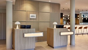 Un área de recepción moderna de hotel con dos mostradores, un cartel que dice "Marriott Bonvoy" y un bar al fondo.