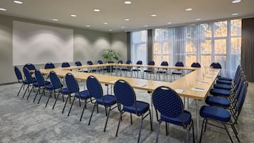 Une salle de conférence avec une longue table et des chaises bleues, de grandes fenêtres et une plante.