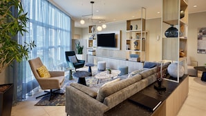 Una sala de estar moderna con sofá, sillón y mesa de centro, un televisor montado en la pared y una estantería con objetos decorativos.