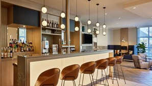 Un área de bar moderna con una barra larga, varios taburetes y una amplia variedad de botellas y copas.