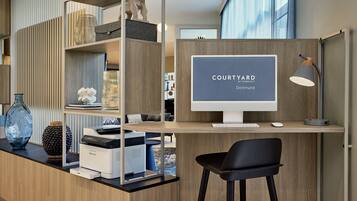 Een moderne kantoorruimte met een houten bureau, een computermonitor en een printer. Er staat een zwarte stoel en decoratieve objecten op de planken.