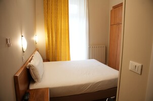 Cama bem arrumada com lençóis brancos, cabeceira de madeira e mesa de cabeceira com controle remoto.