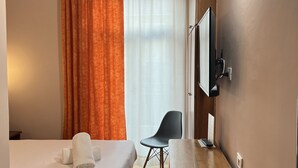 Habitación de hotel con cama, escritorio, silla, televisor y ventana con cortinas.