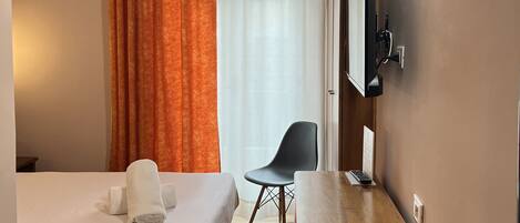 A hotel room with a bed, a desk, a chair, a TV, and a window with curtains.