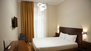 Habitación de hotel con una cama grande, un escritorio de madera, una silla y un televisor instalado en la pared.