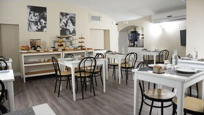 Un comedor moderno con mesas y sillas blancas, una zona de cocina con electrodomésticos y obras de arte en las paredes.
