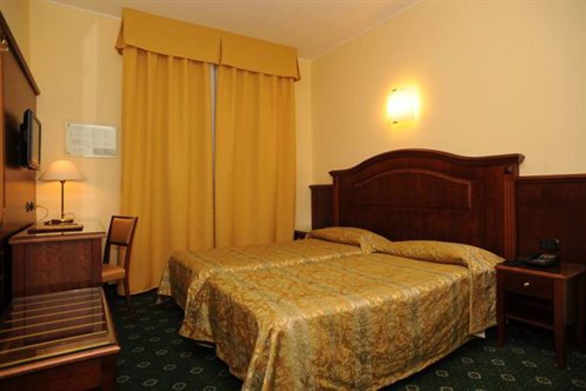 Habitación de hotel con cama doble, escritorio con lámpara, silla y mesita de noche con teléfono.