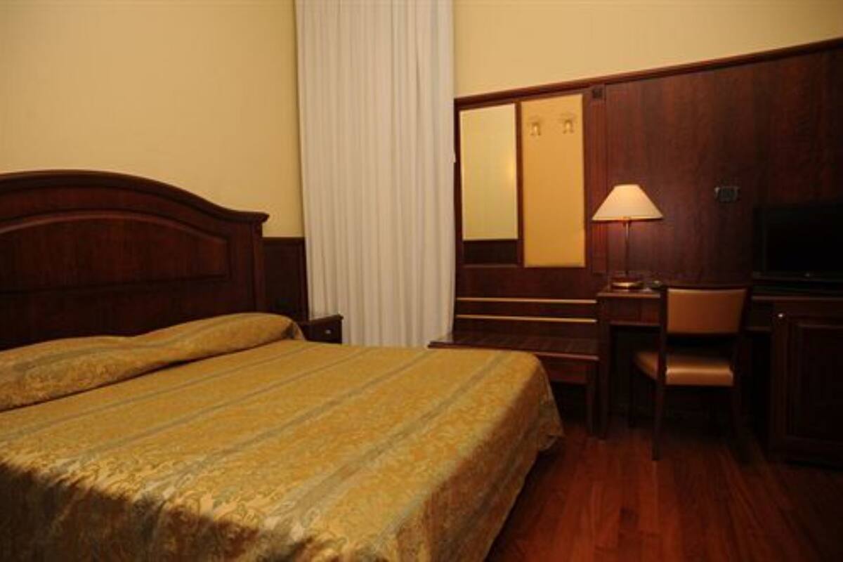 Habitación de hotel con una cama grande, un escritorio, una silla, un televisor y un espejo.