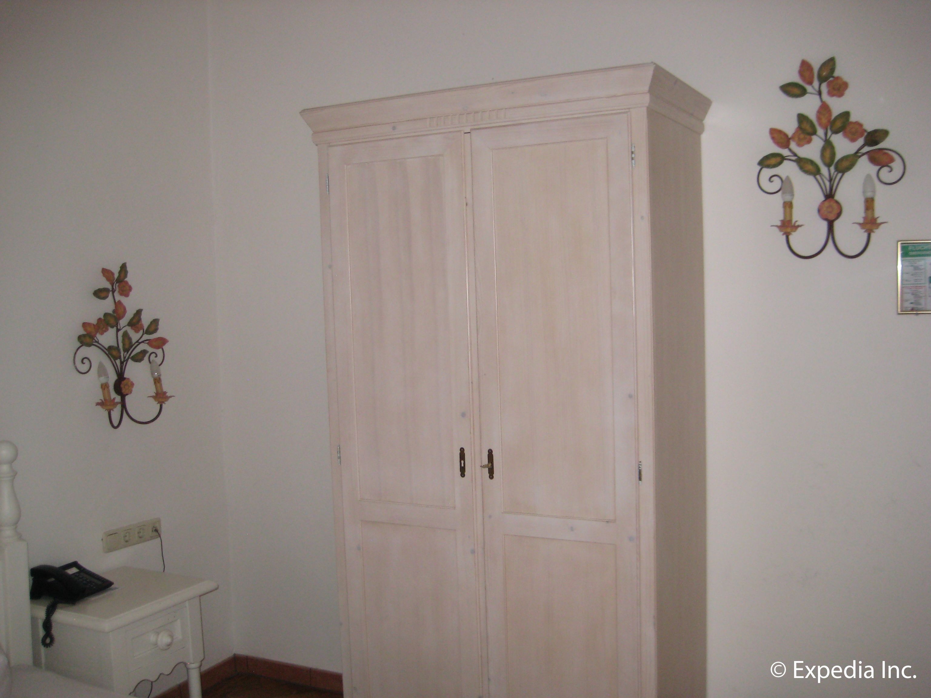 A room with a large wardrobe, a bedside table with a lamp, and a wall decoration.
