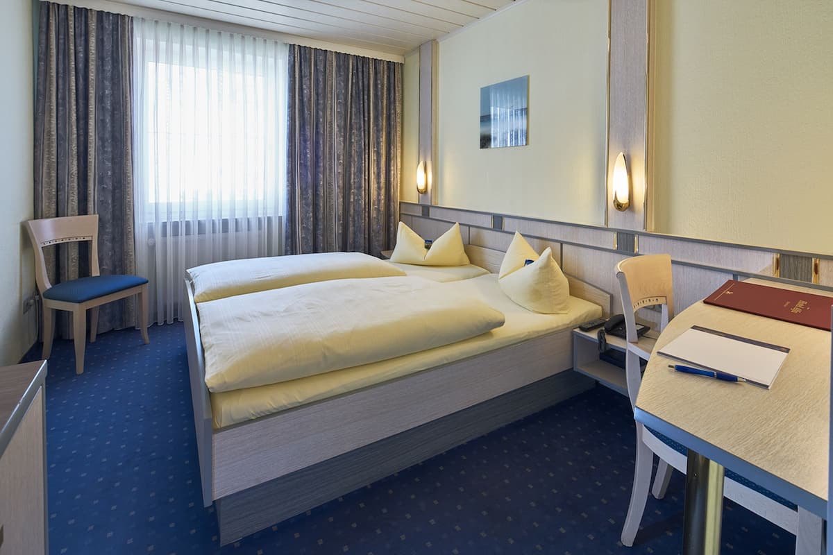 Een hotelkamer met een groot bed, een bureau met stoel, een fauteuil en een raam met gordijnen.