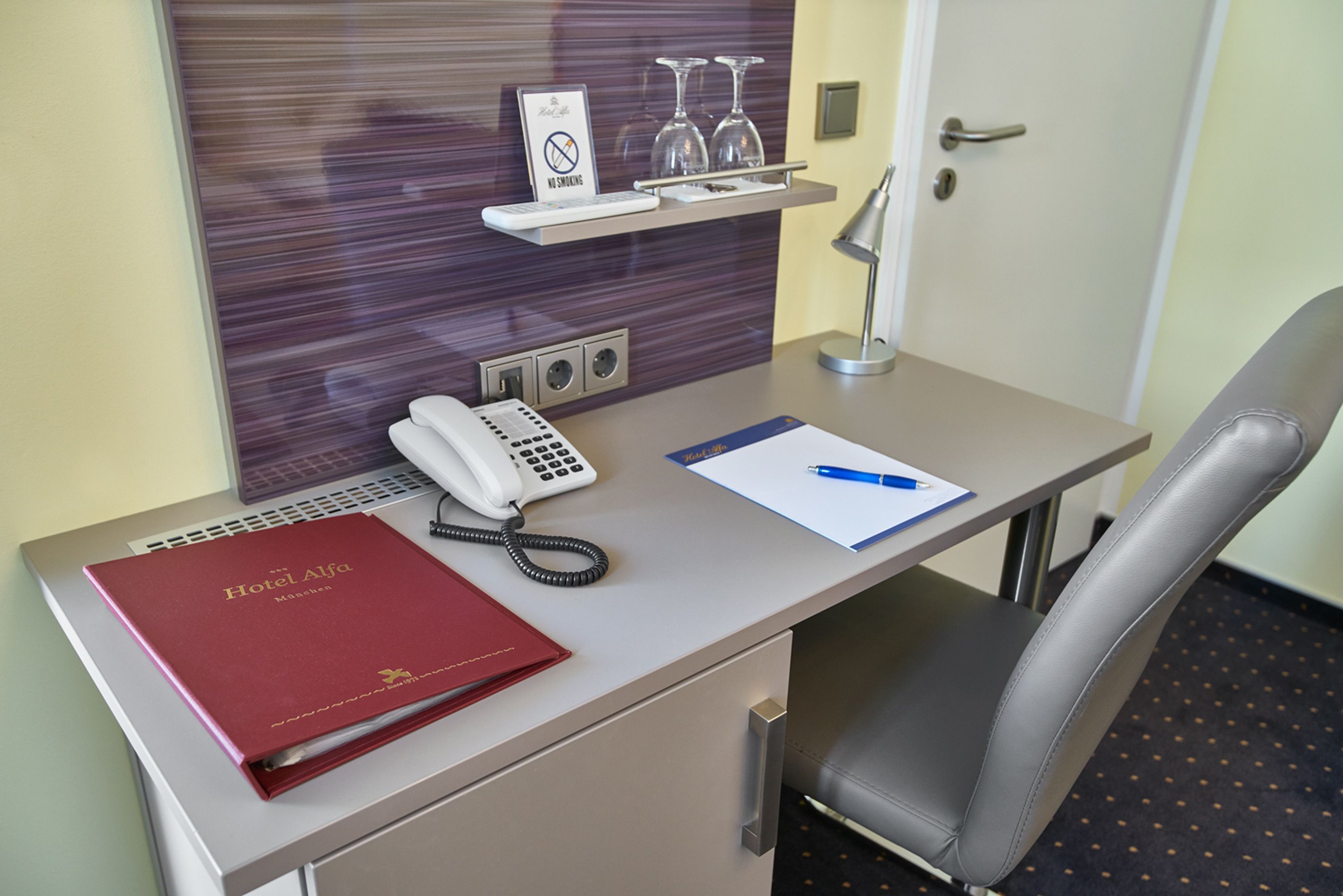 Mostrador de hotel con teléfono, una carpeta roja, un bolígrafo y un bloc de notas.