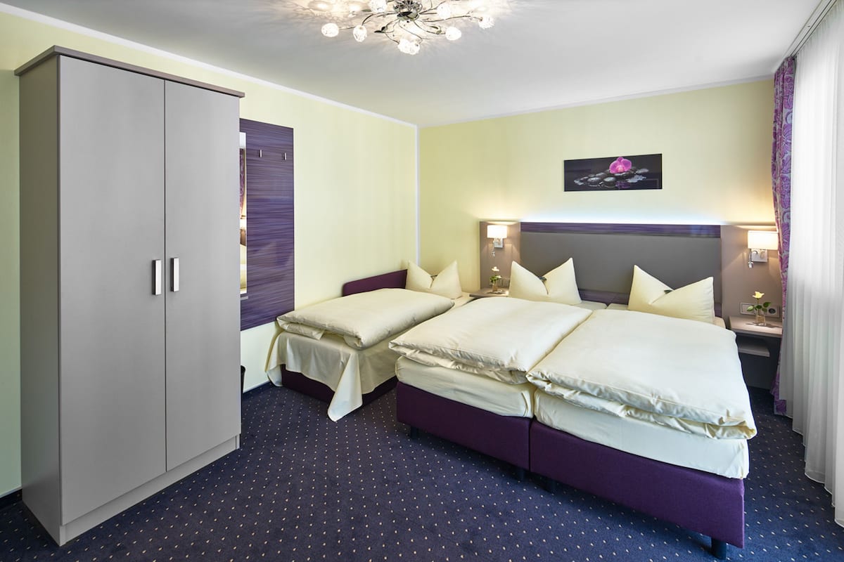 Een hotelkamer met twee bedden, een kledingkast, een plafondlamp en een kunstwerk aan de muur.