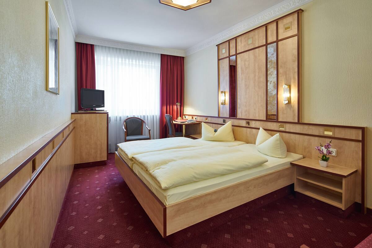 Een hotelkamer met een groot bed, een bureau met stoel, een televisie en een kledingkast.