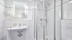 Un baño moderno con ducha envuelta en vidrio, un lavamanos blanco y un espejo sobre él.