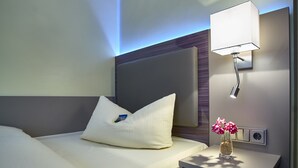 Una cama bien hecha con una almohada y una mesita de noche con un florero.