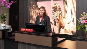 A reception desk with a digital screen displaying a dog, a vase with flowers, and a fruit bowl. - Hotel Munich City (Munich)