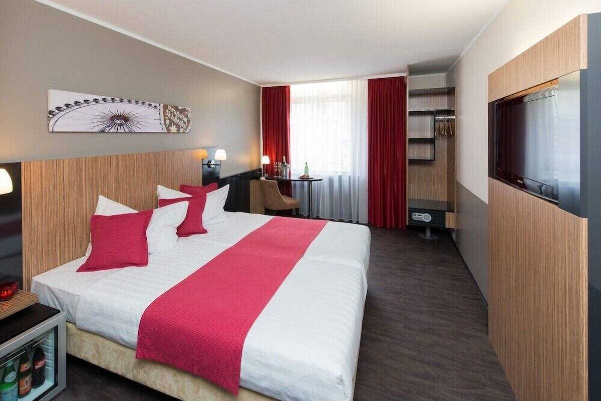 Una habitación de hotel con una cama grande, un televisor, un escritorio con una silla y una mesita con una botella.