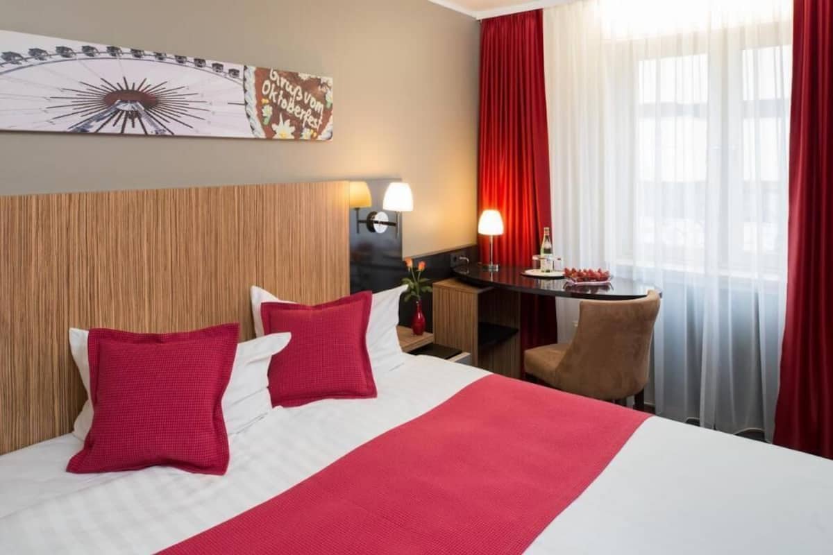 Una habitación de hotel con una cama, un escritorio, una silla, una lámpara y una ventana con cortinas.