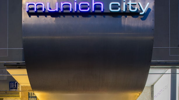 A building entrance with a neon sign reading "Munich City" and a revolving door. - Hotel Munich City (Munich)