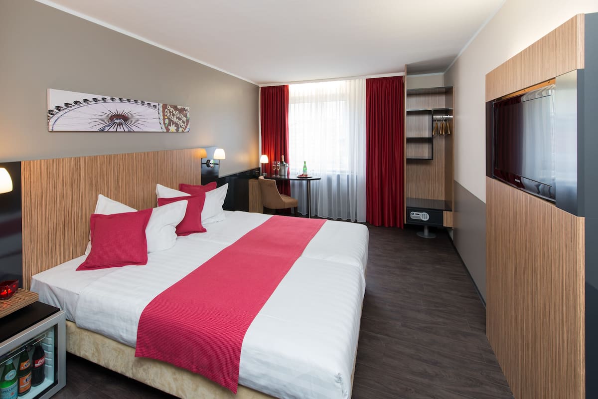Una habitación de hotel con una cama grande, un escritorio, una silla, un televisor y un minibar.