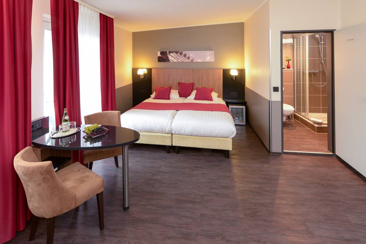 Habitación de hotel con cama, una mesa con sillas, una cortina roja y zona de ducha.