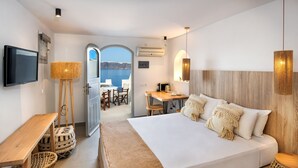 A modern hotel room with a large bed, a desk, a TV, and a view of the sea.