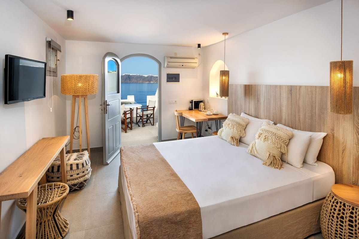 A modern hotel room with a large bed, a desk, a TV, and a view of the sea.