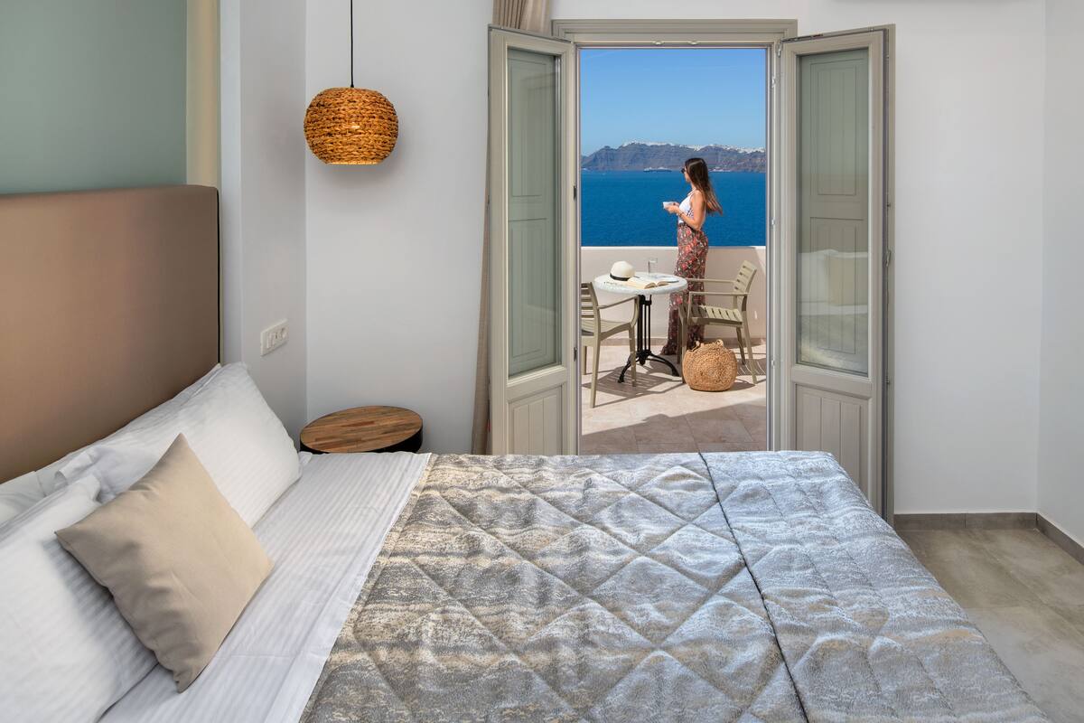 A bedroom with a bed, a bedside table, a chair, and a view of the sea through an open door.