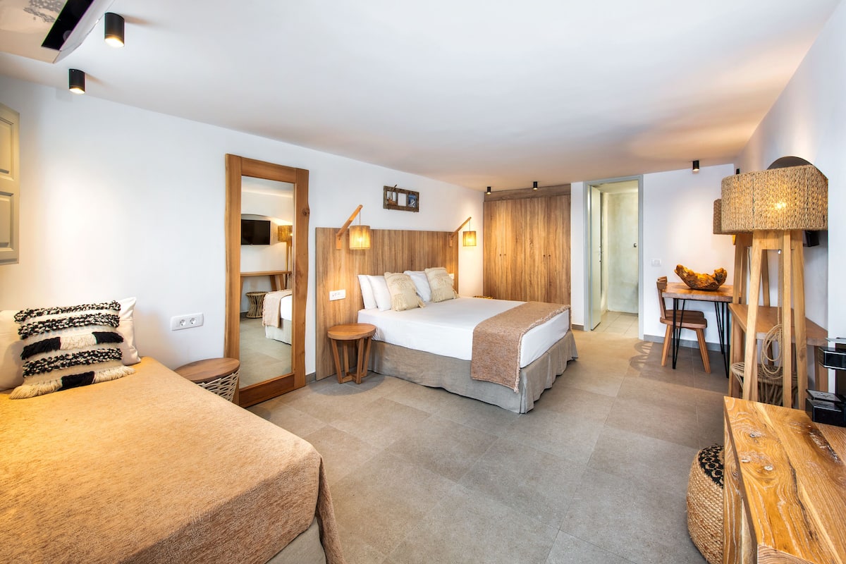 A modern hotel room with a large bed, a small desk, and a dining area.