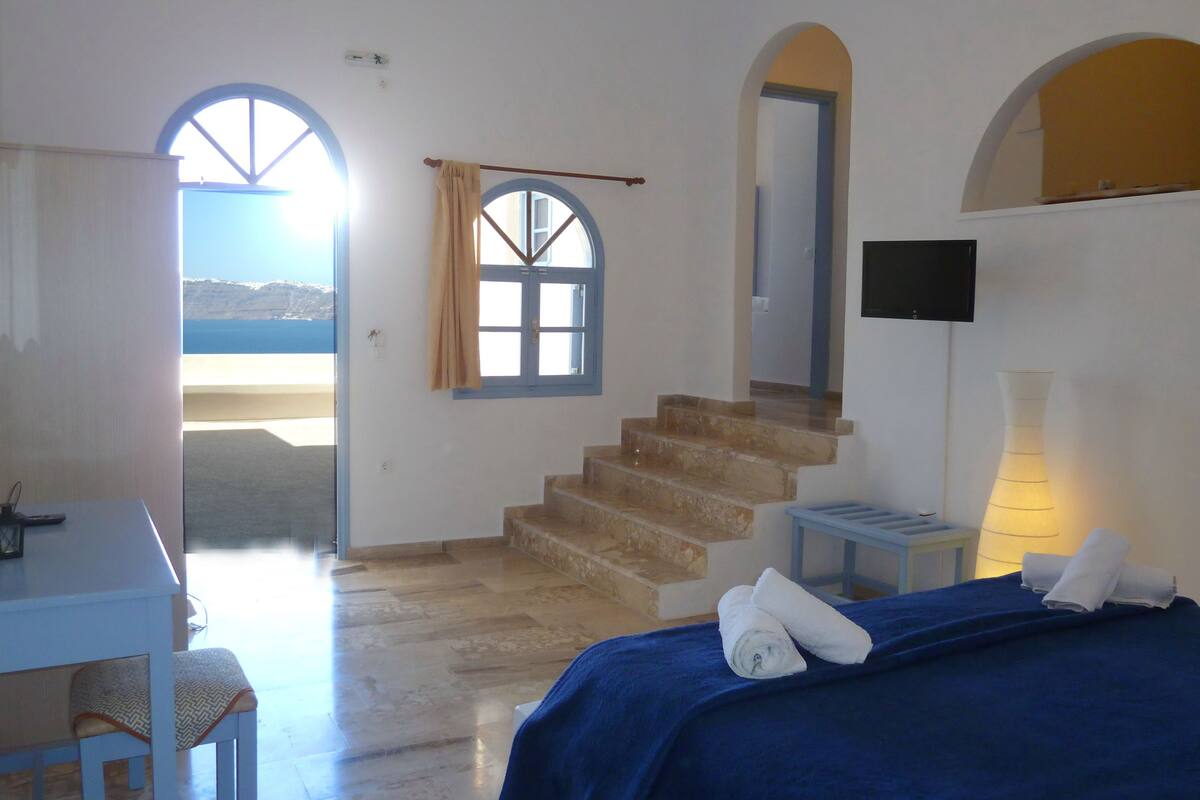 A room with a bed, a desk, a chair, a TV, a lamp, and a staircase leading to another room.