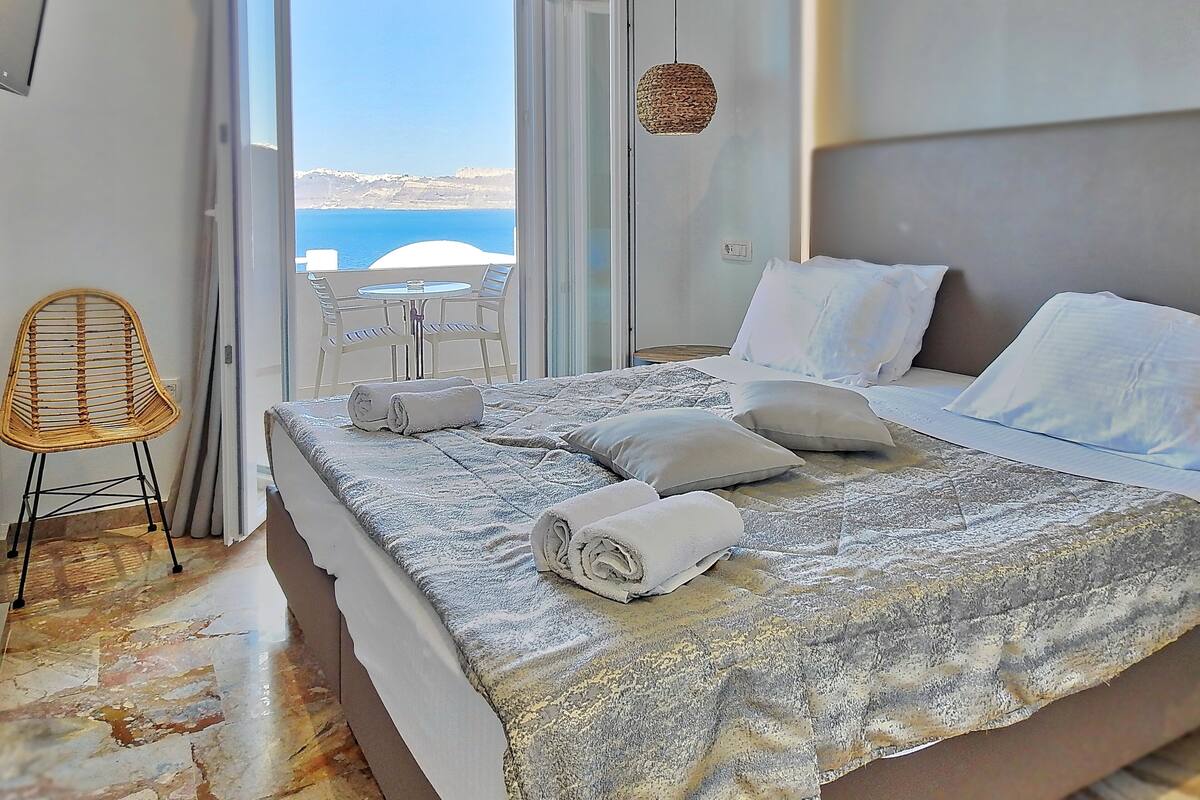 A bedroom with a bed, a chair, and a view of the sea.