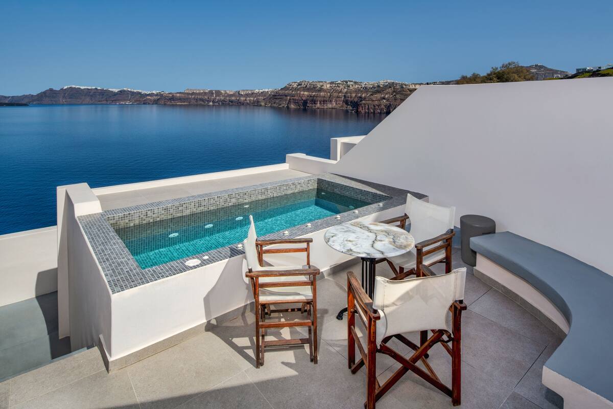 A rooftop terrace with a swimming pool, wooden chairs, and a table.