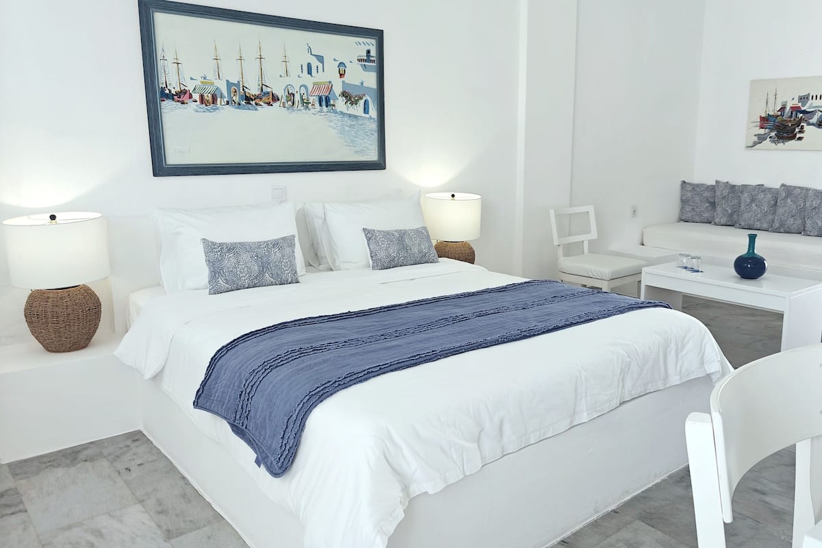 A modern, minimalist bedroom with a large bed, white furniture, and two wall-mounted paintings.