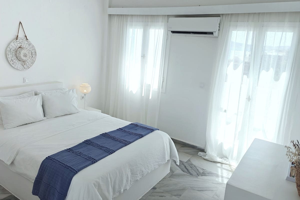 A minimalist bedroom with a bed, bedside lamps, and a wall-mounted air conditioner.