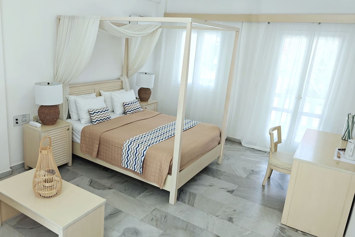 A neatly arranged bedroom with a four-poster bed, bedside tables, a chair, and a desk.