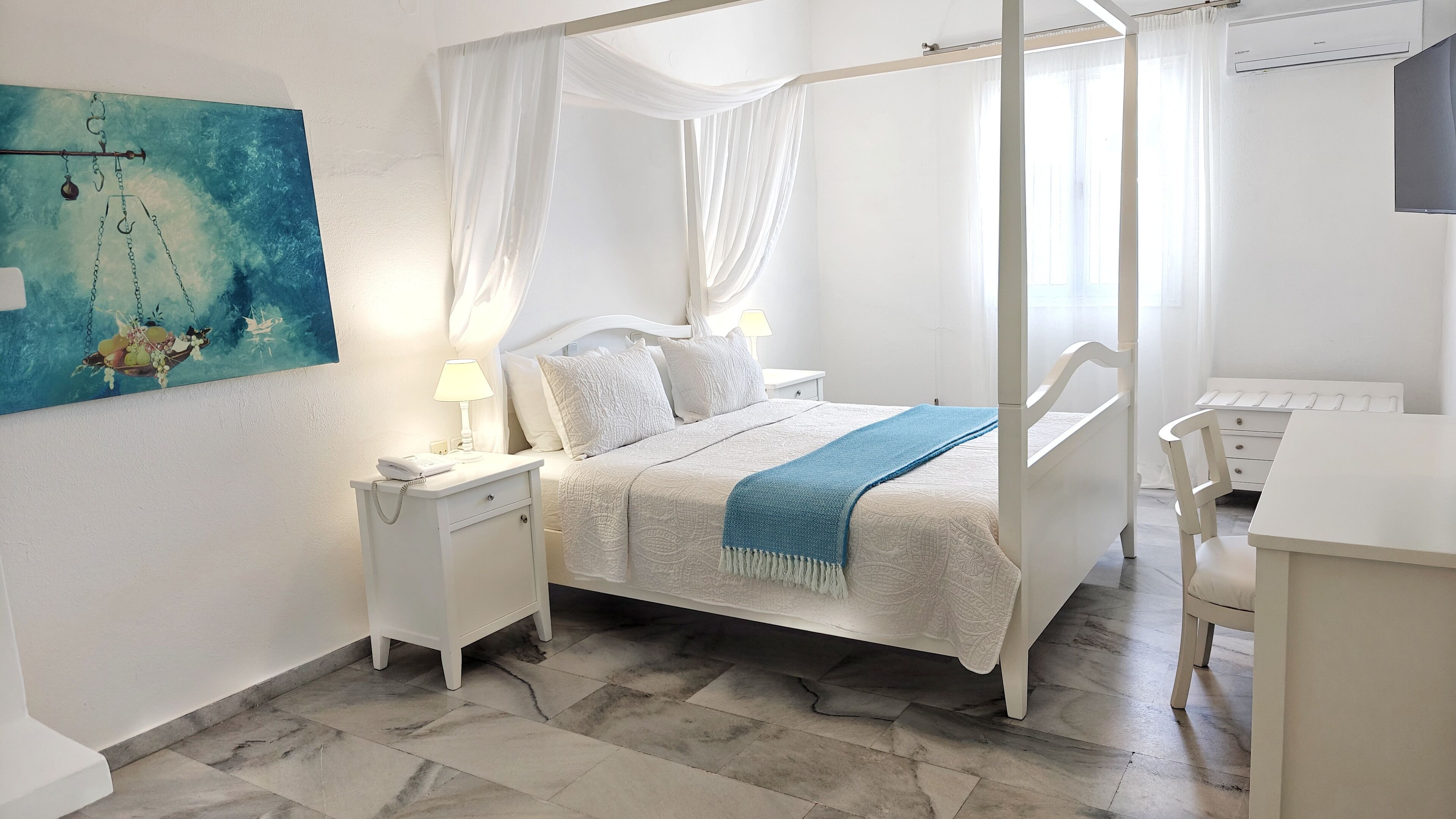 A bedroom with a four-poster bed, a nightstand with a lamp, a desk with a chair, and a painting on the wall.