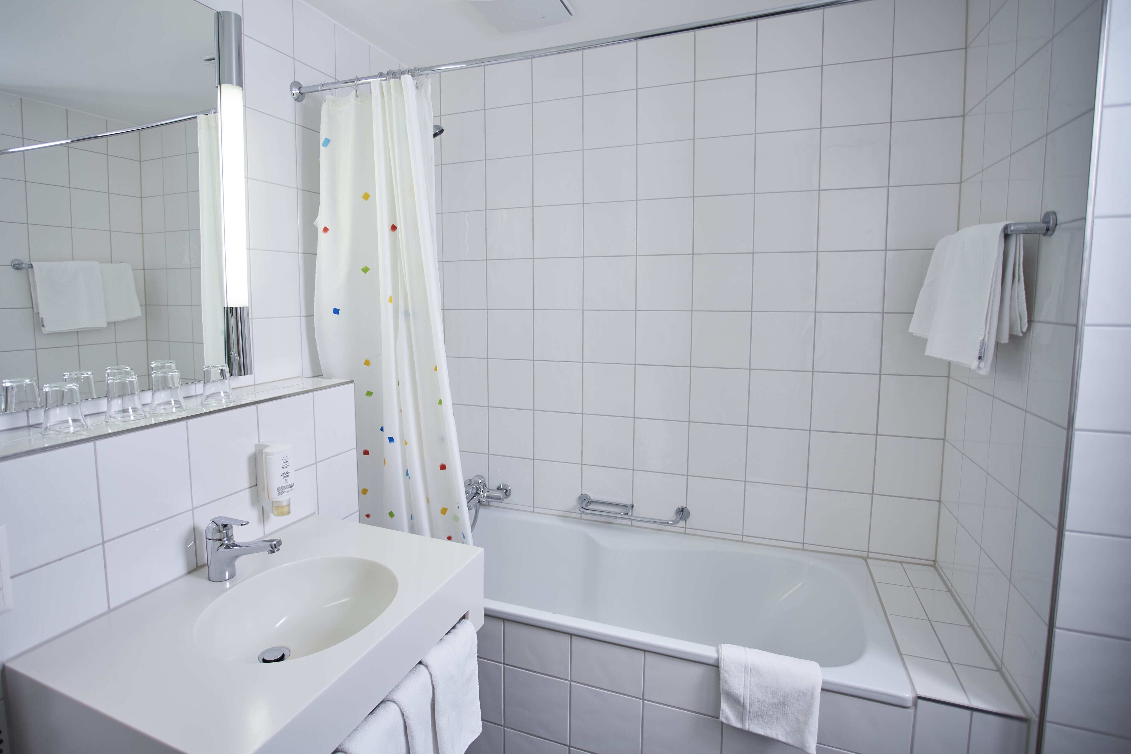 A modern bathroom with a white sink, mirror, and bathtub.