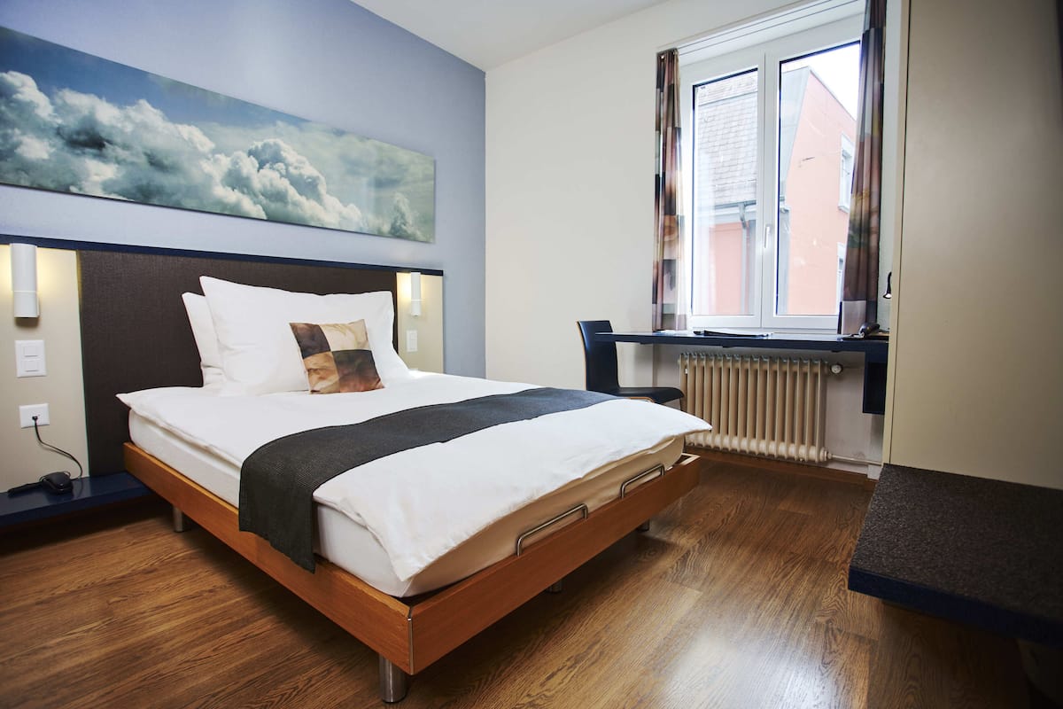 Une chambre d’hôtel moderne avec un lit en bois, un bureau et une grande fenêtre.