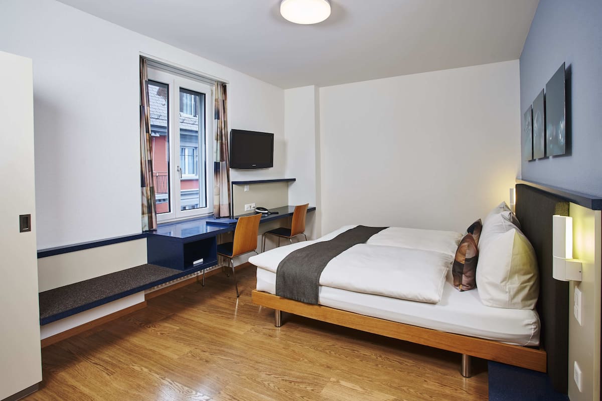 Une chambre à coucher avec un lit, un bureau, une chaise et un téléviseur fixé au mur.