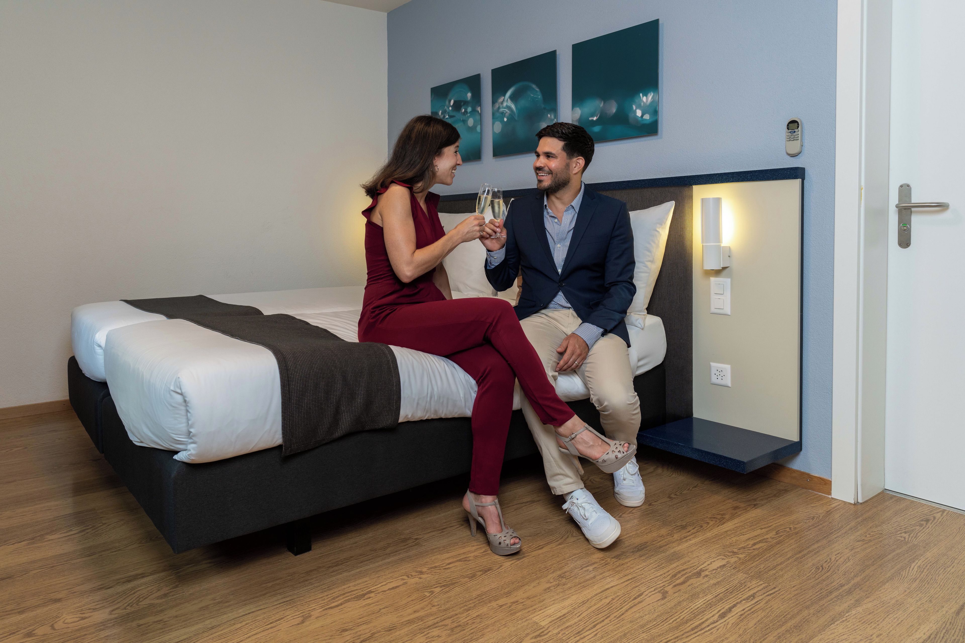 A modern hotel room with a bed, a nightstand, and a wall-mounted light fixture.