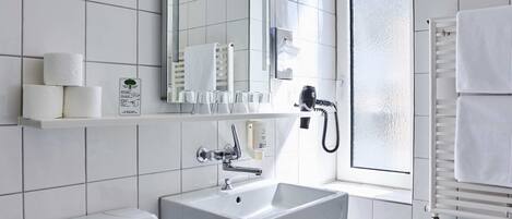 A modern bathroom with a white toilet, a sink, and a mirror. There is a window with a view of the outside, and a towel rack with towels.