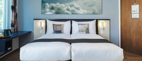 A double bed with a dark headboard and white bedding, a wall-mounted artwork of clouds, and a wooden door with a sign.