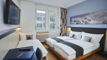 Habitación de hotel con cama, escritorio, silla, televisor y ventana con cortinas.