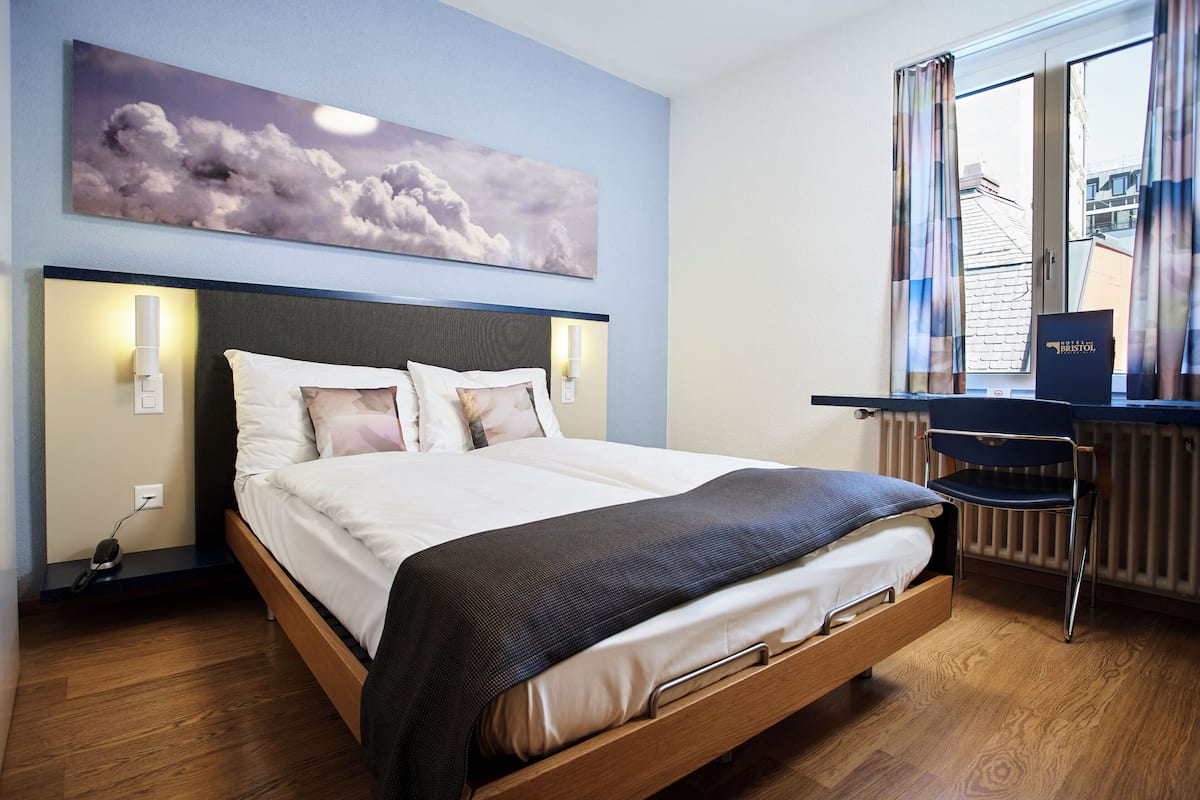 Une chambre d’hôtel avec un lit, des lampes de chevet, un bureau avec une chaise et une fenêtre avec des rideaux.