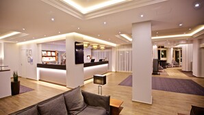 A modern hotel lobby with a reception desk, seating area, and a bar. - Kurpark-Hotel Bad Dürkheim (Bad Durkheim)