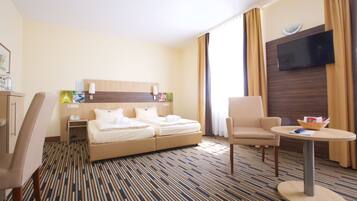 Ein Hotelzimmer mit einem Bett, einem Schreibtisch, einem Sessel, einem Fernseher und einem kleinen Tisch.