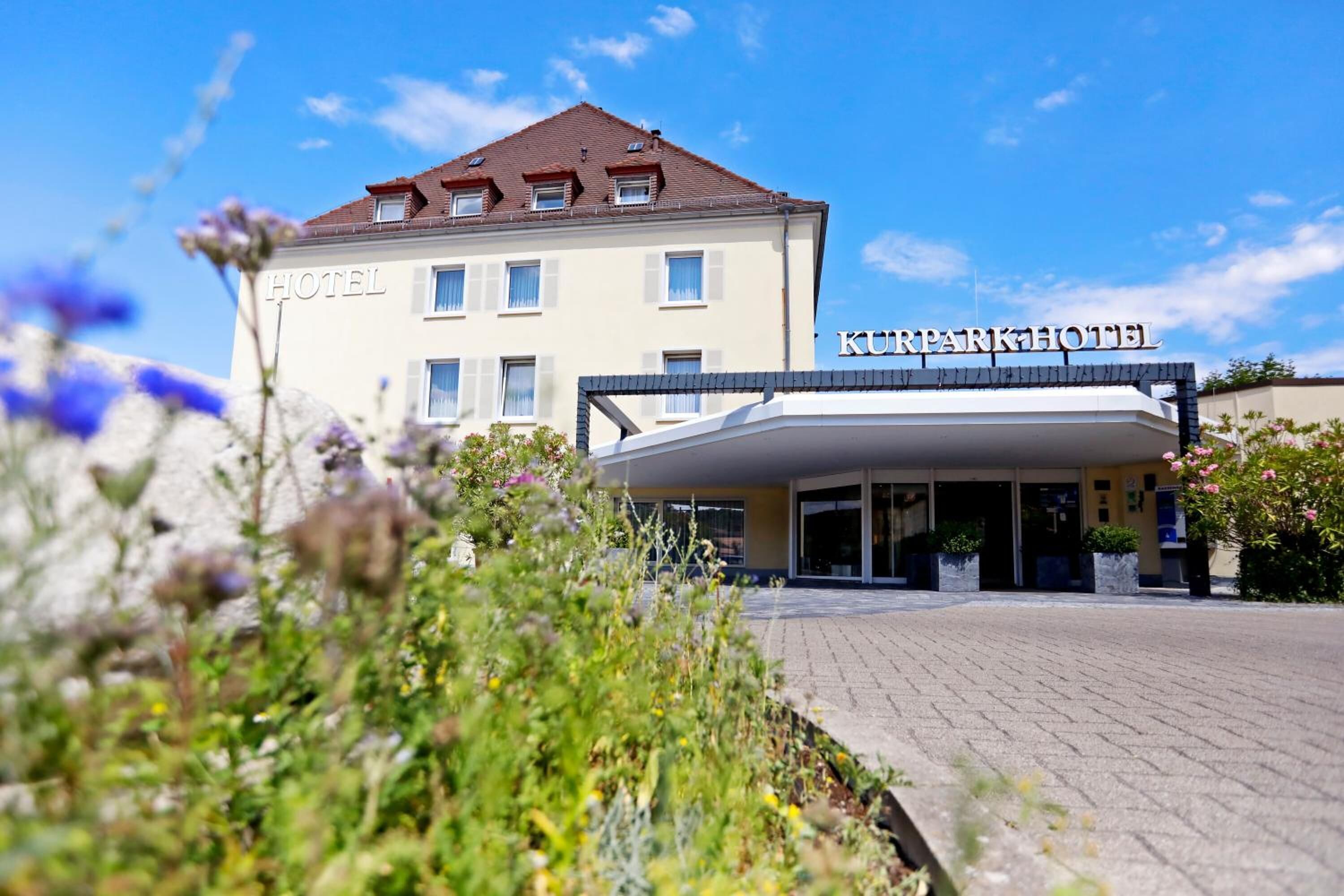 Un hotel con un cartel que dice "KURPARKHOTEL" y una zona de entrada techada.
