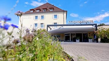 Un hôtel avec une enseigne indiquant « KURPARKHOTEL » et une zone d’entrée abritée.
